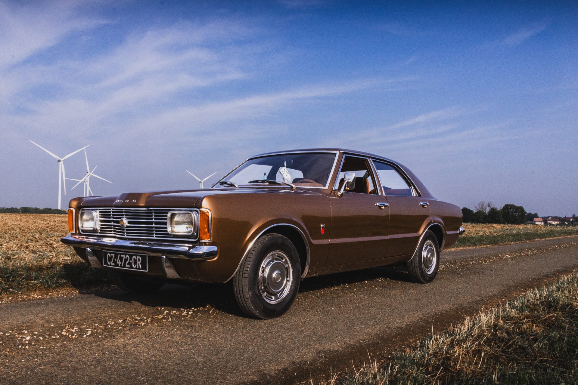 Une vieille Ford marron dans un champ avec des éoliennes en fond